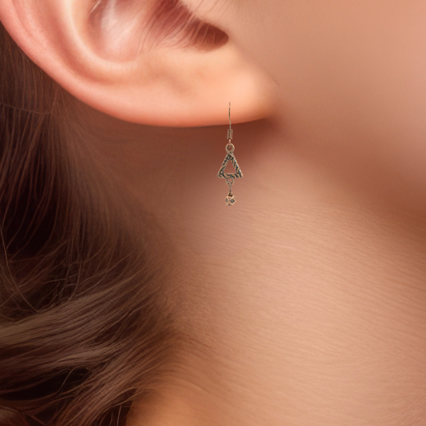 Close-up of a person wearing an antique copper bohemian style dangling earring with a soft background