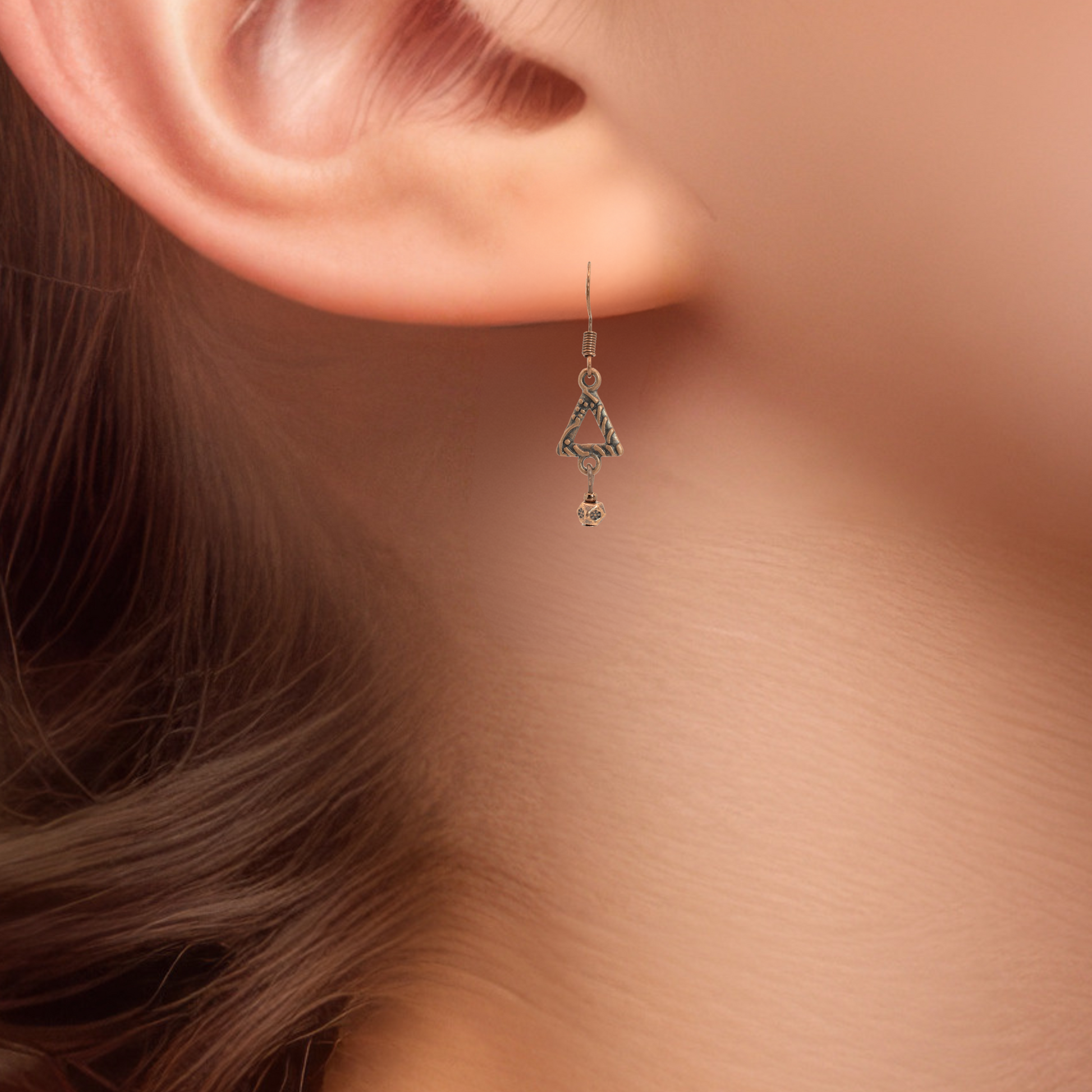 Close-up of a person wearing an antique copper bohemian style dangling earring with a soft background