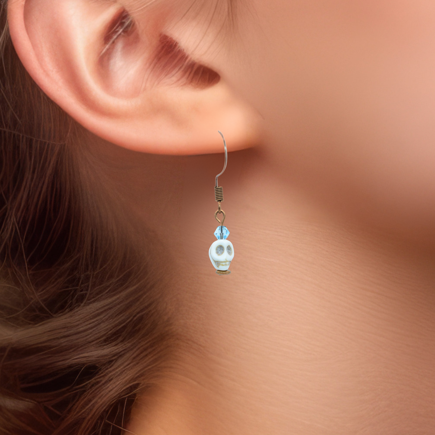 Close-up of an ear wearing a skull-shaped earring with light blue Autrian crystal beads