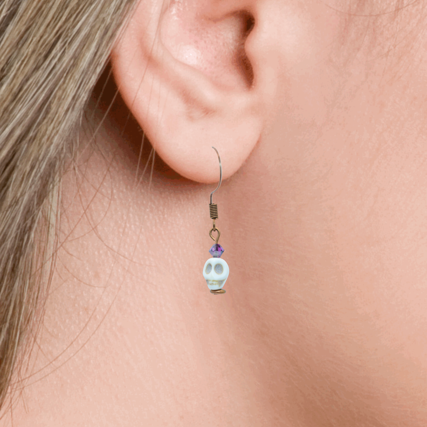 Close-up of an ear wearing a skull-shaped earring with dark pink crystal beads.