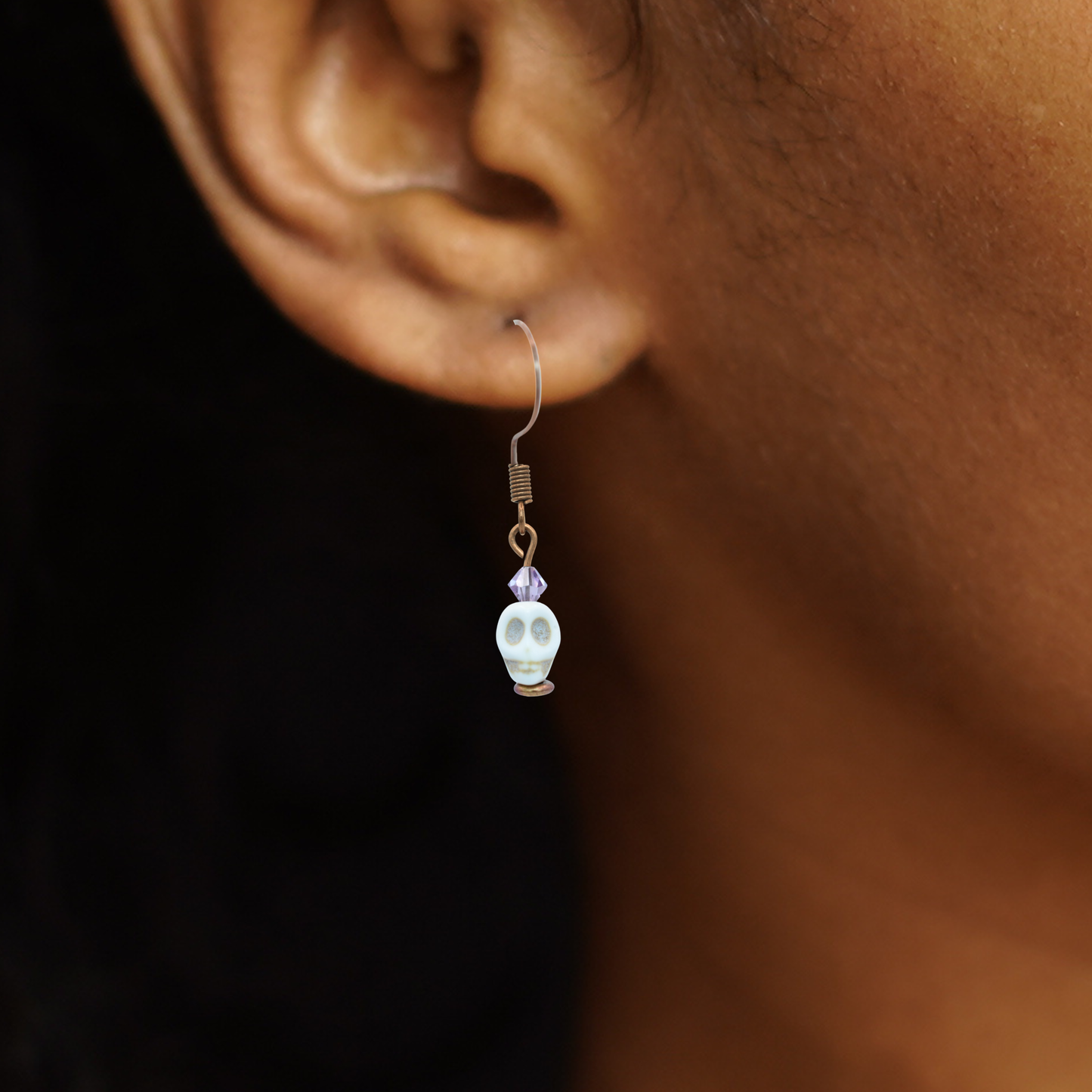Close-up of an ear wearing a skull-shaped earring with a dark background