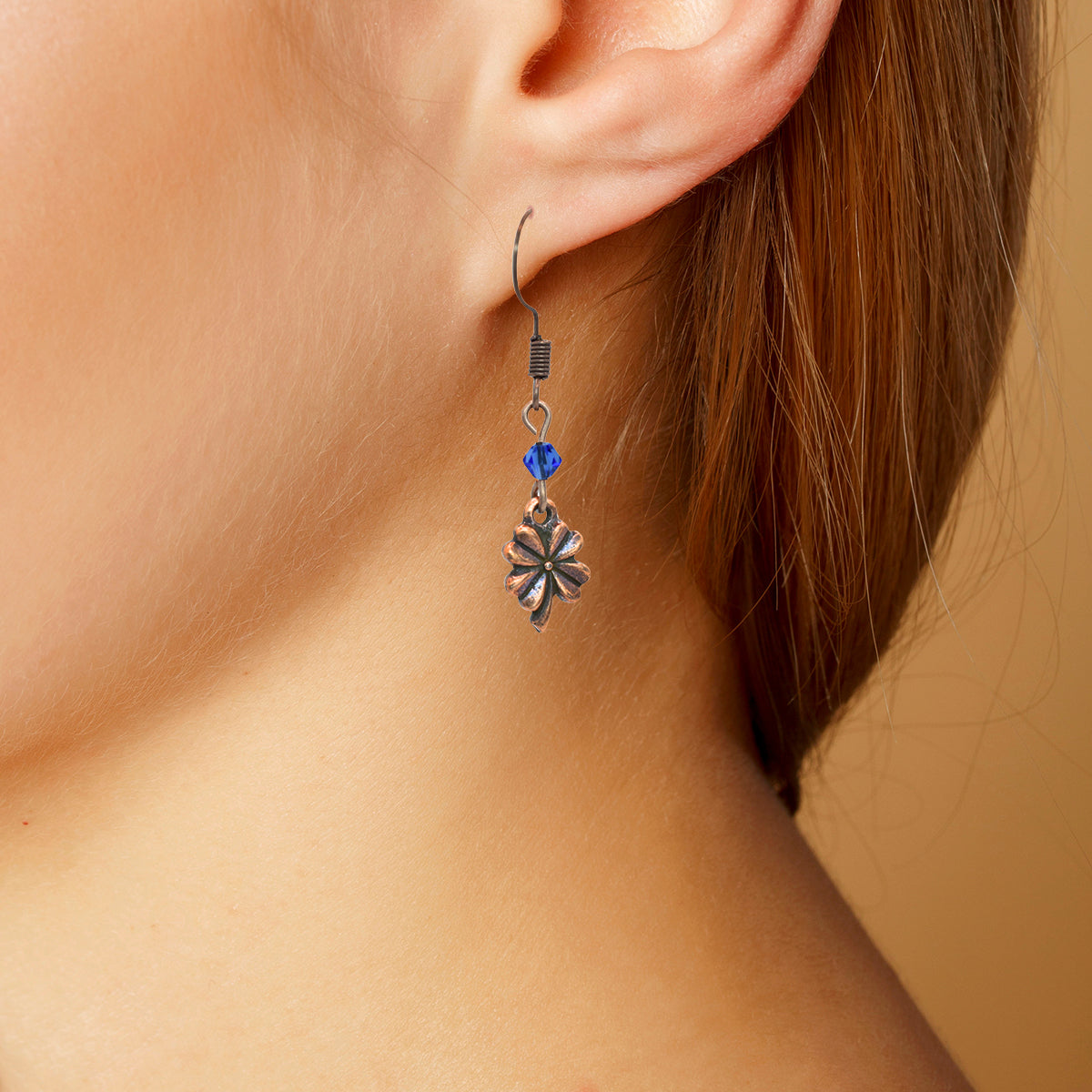 Close-up of an earring with a blue crystal bead on a beige background