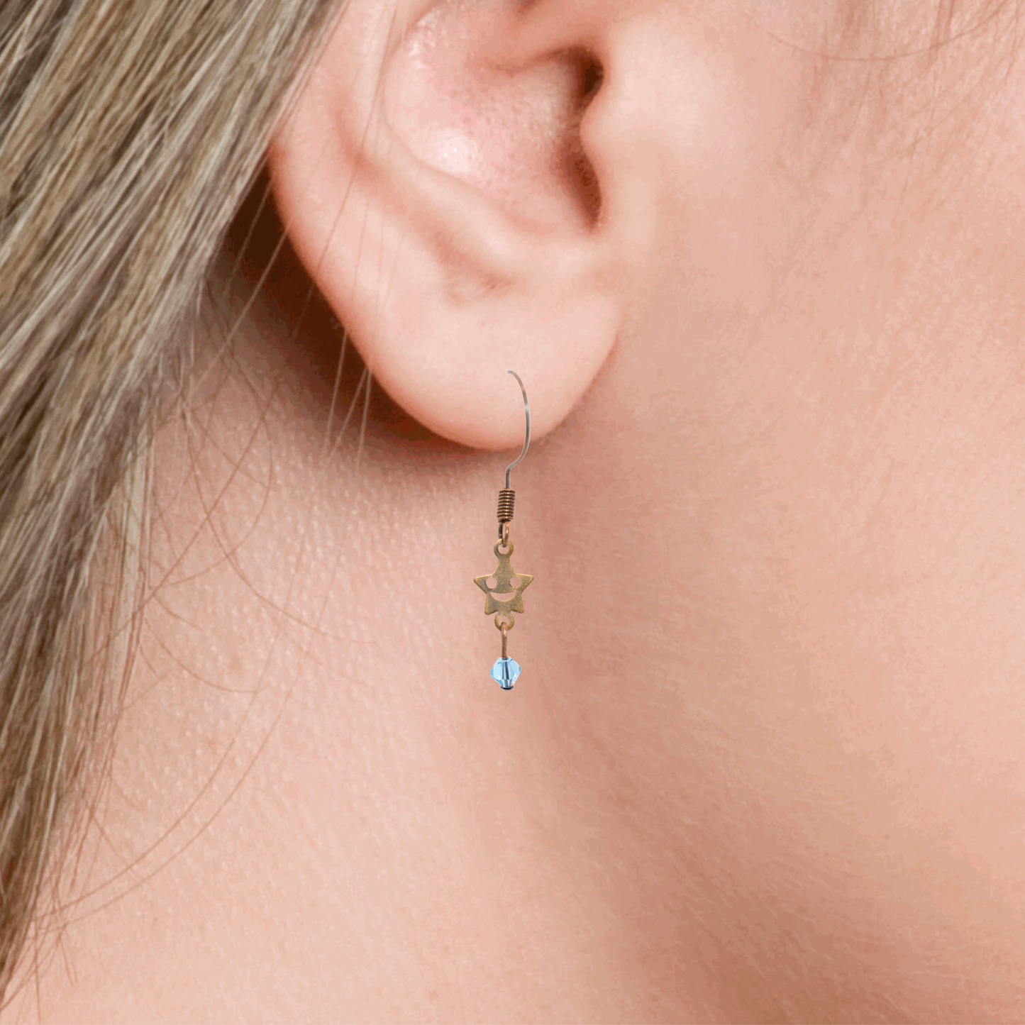 Close-up of an ear wearing a star-shaped earring with a blue crystal bead.