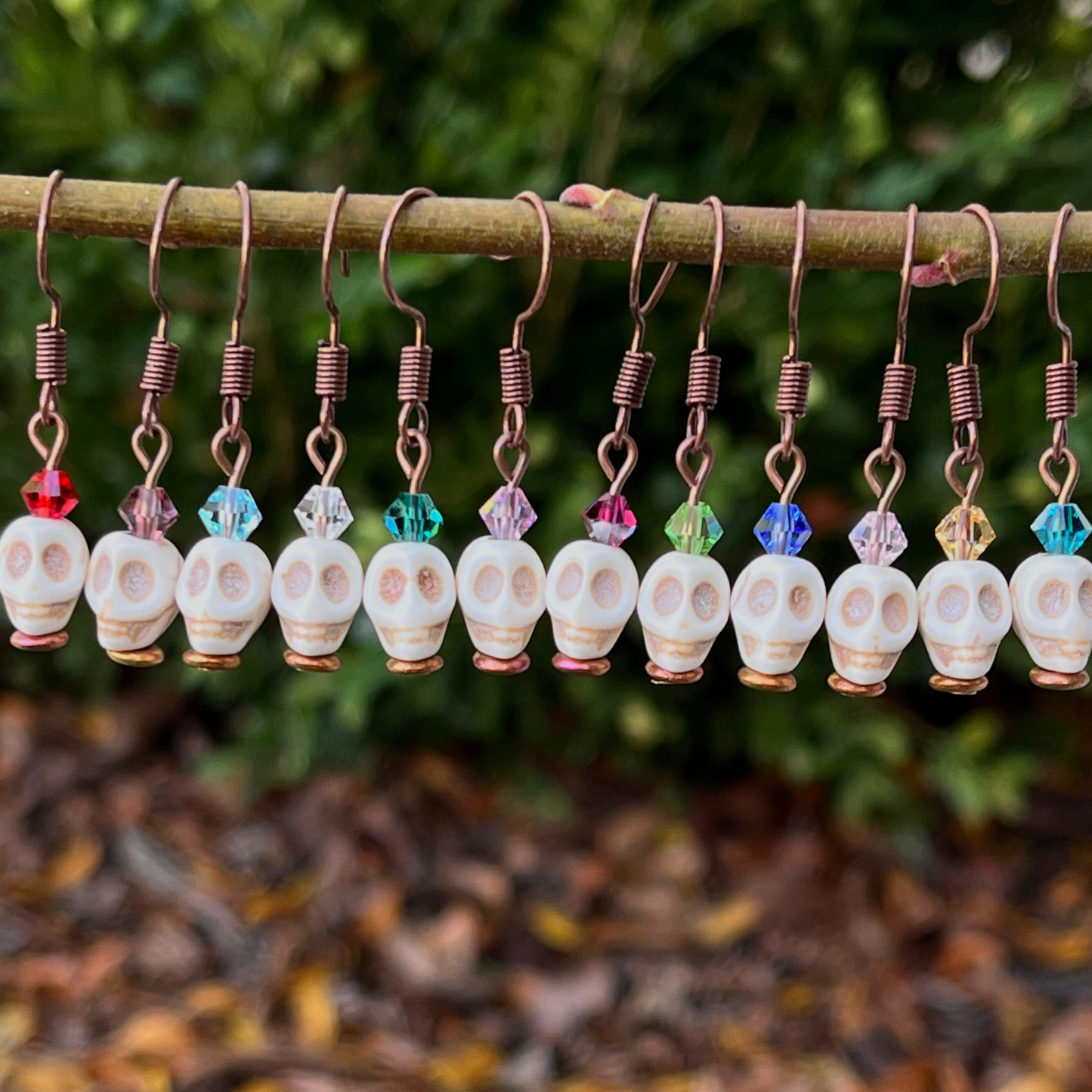 Skull-shaped earrings with colorful beads hanging on a branch against a natural background.