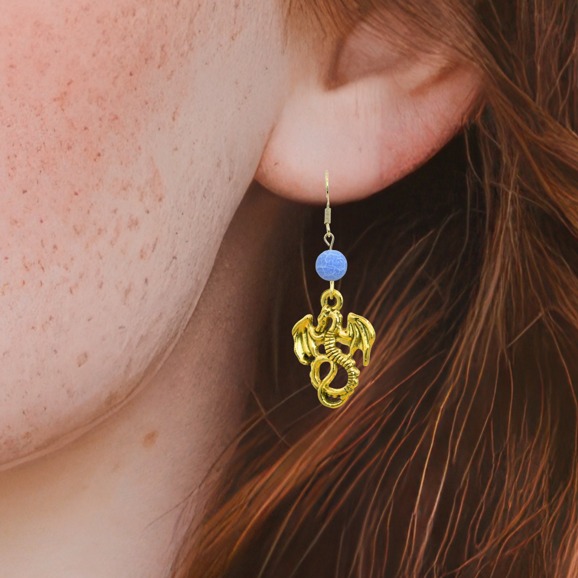 Gold dragon-shaped earring with a blue bead on an ear