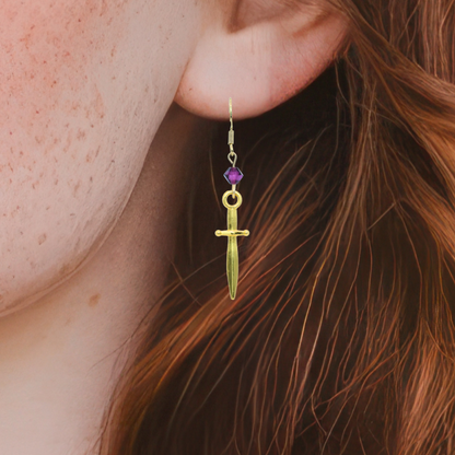 Gold earring with a purple crystal bead worn by a person with red hair.