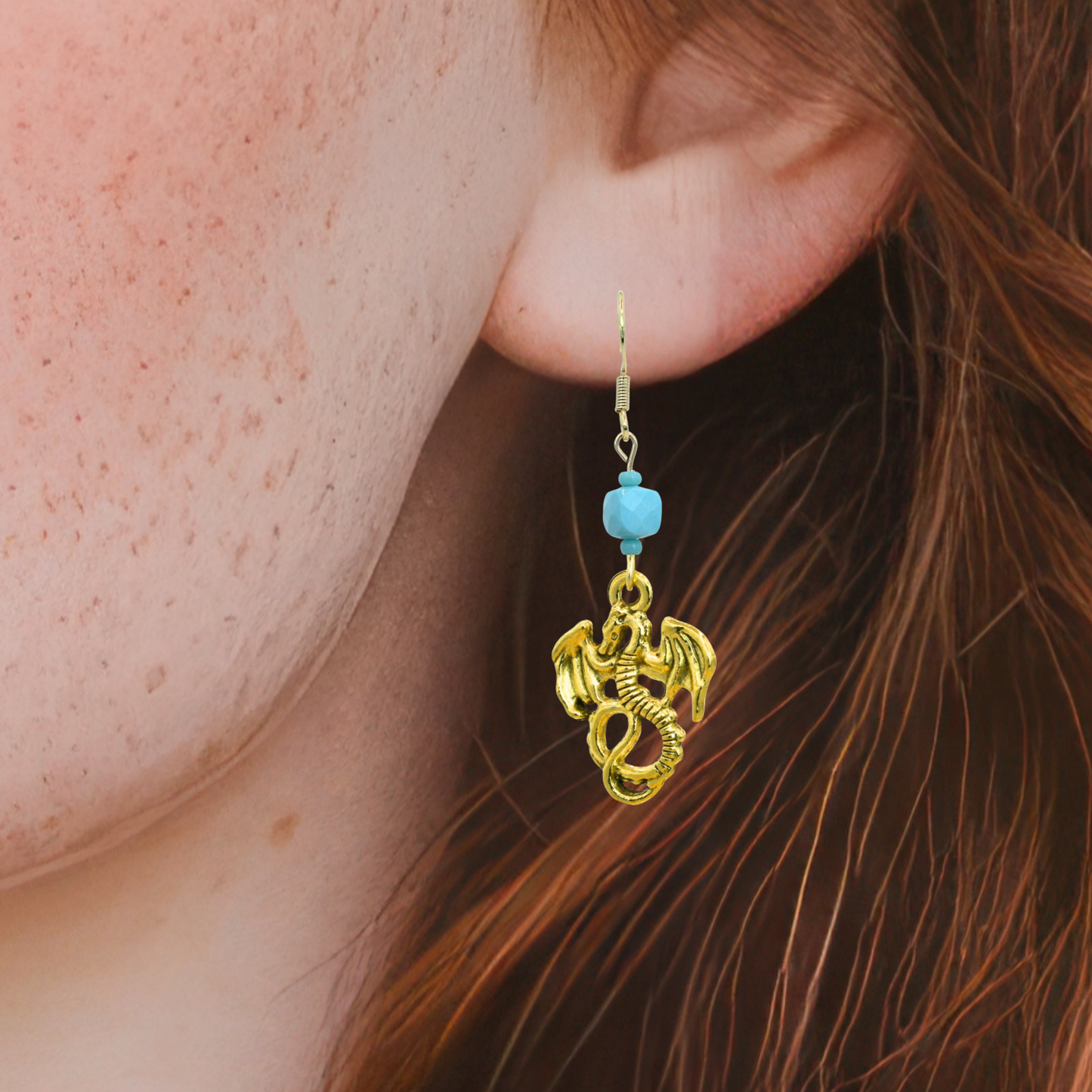 Gold dragon-shaped earring with a blue bead worn by a person with red hair.