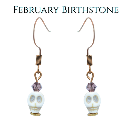 Skull-shaped earrings with purple crystal beads on a white background, labeled 'February Birthstone'.