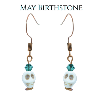 Earrings with white skull  beads and dark green crystal beads on a white background, labeled 'May Birthstone'.