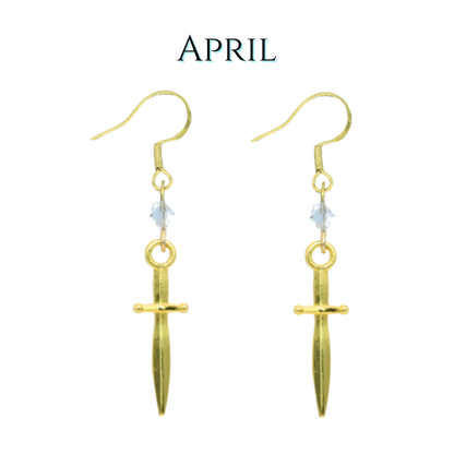 Gold dagger-shaped earrings with a clear crystal beads on a white background, labeled 'April'.