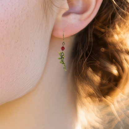 Close-up of a person wearing a green fairy earring with a red gemstone.