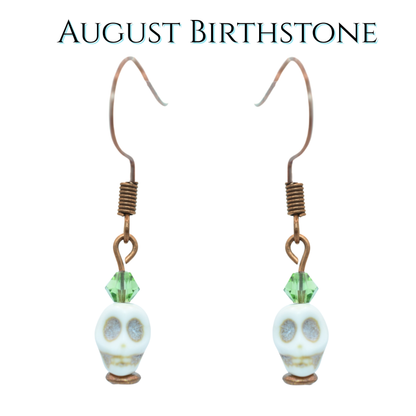Skull-shaped earrings with green crystal beads on a white background, labeled 'August Birthstone'.