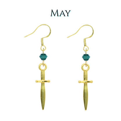 Gold dagger-shaped earrings with green crystal beads on a white background, labeled 'MAY'.