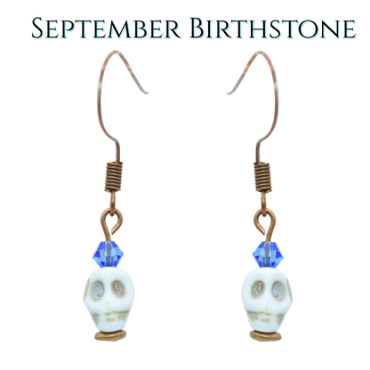 Skull-shaped earrings with blue crystal beads on a white background, labeled 'September Birthstone'.