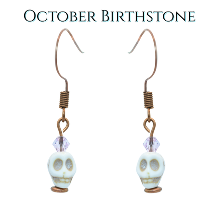 Skull-shaped earrings with a light pink crystal beads on a white background, labeled 'October Birthstone'.