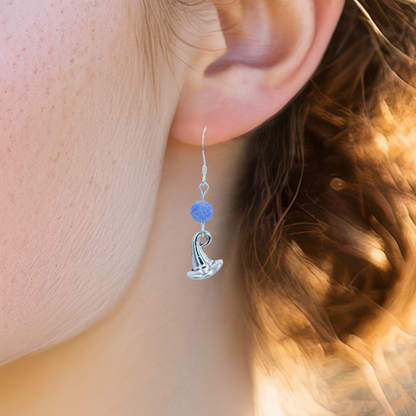 Close-up of an ear wearing a silver earring with a blue agate bead and witch hat charm.