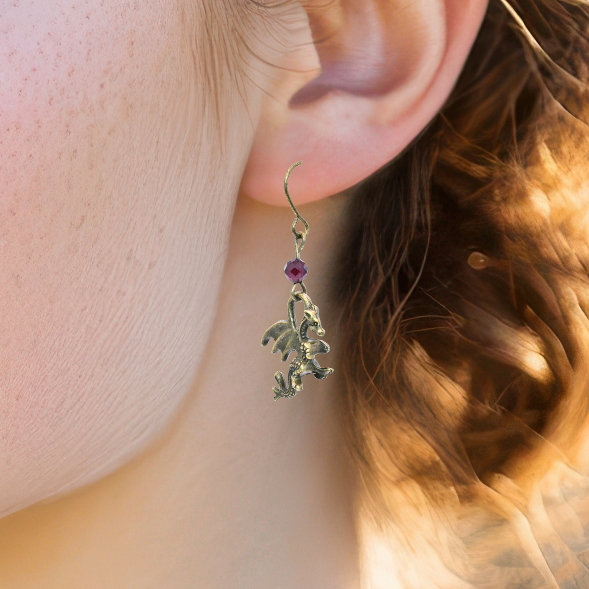 Close-up of a person wearing a dragon-shaped earring with a red gemstone.
