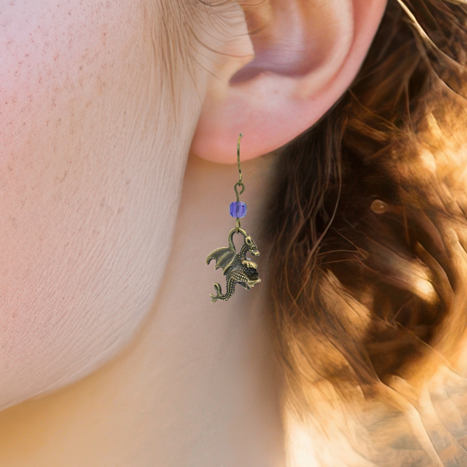 Close-up of an ear wearing a dragon-shaped earring with a purple amethyst bead.