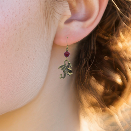 Close-up of an earring with a dragon charm and red gemstone worn by a person.