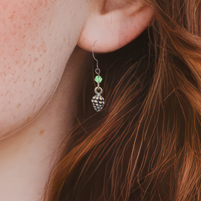 Close-up of an earring with a light green crystal bead worn by a person with red hair.