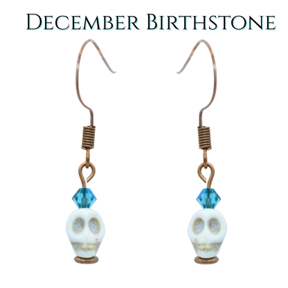 Skull-shaped earrings with teal blue crystal beads on a white background, labeled 'December Birthstone'.