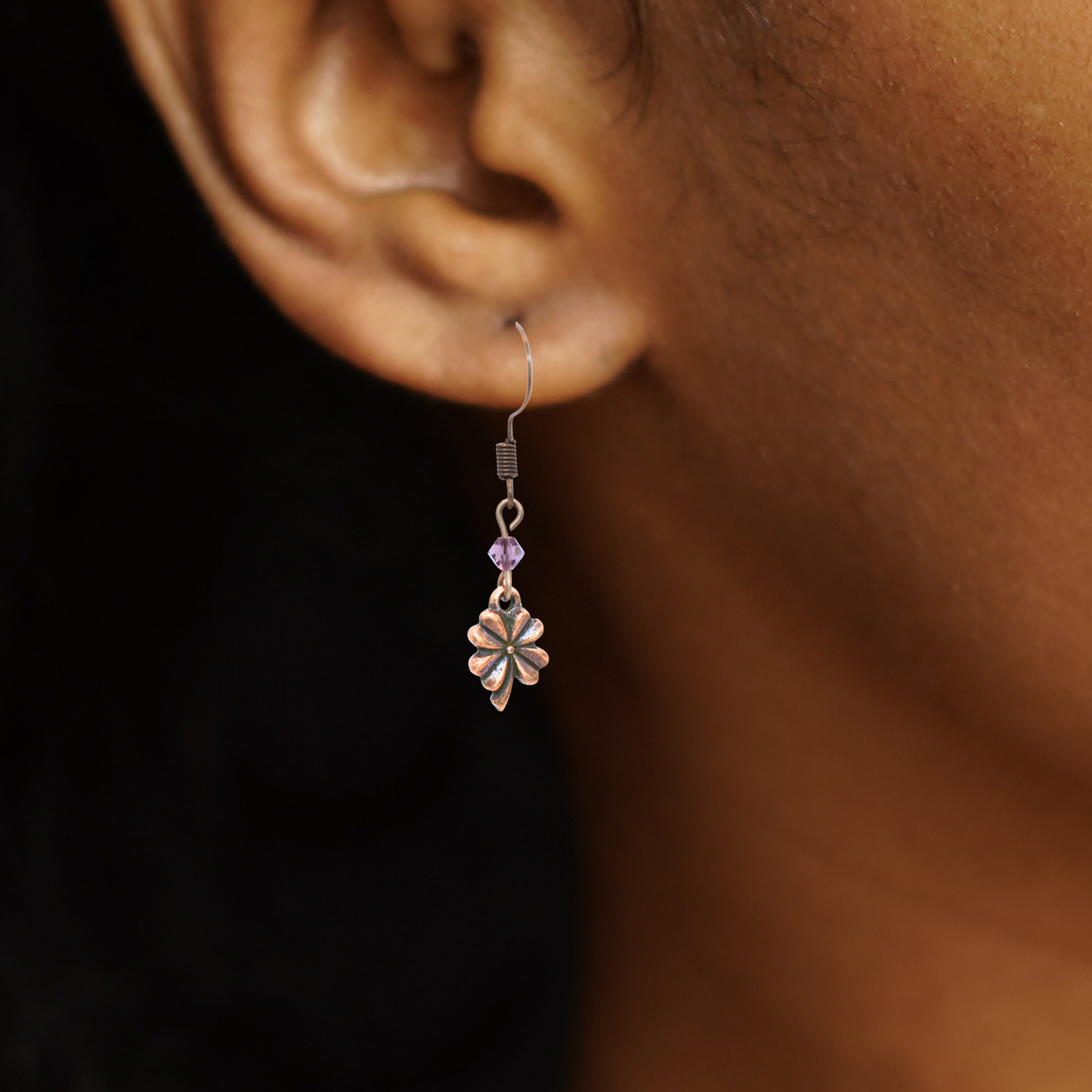 Close up a person wearing earrings featuring antique copper four leaf clover charms and Austrian crystal beads in birthstone colors