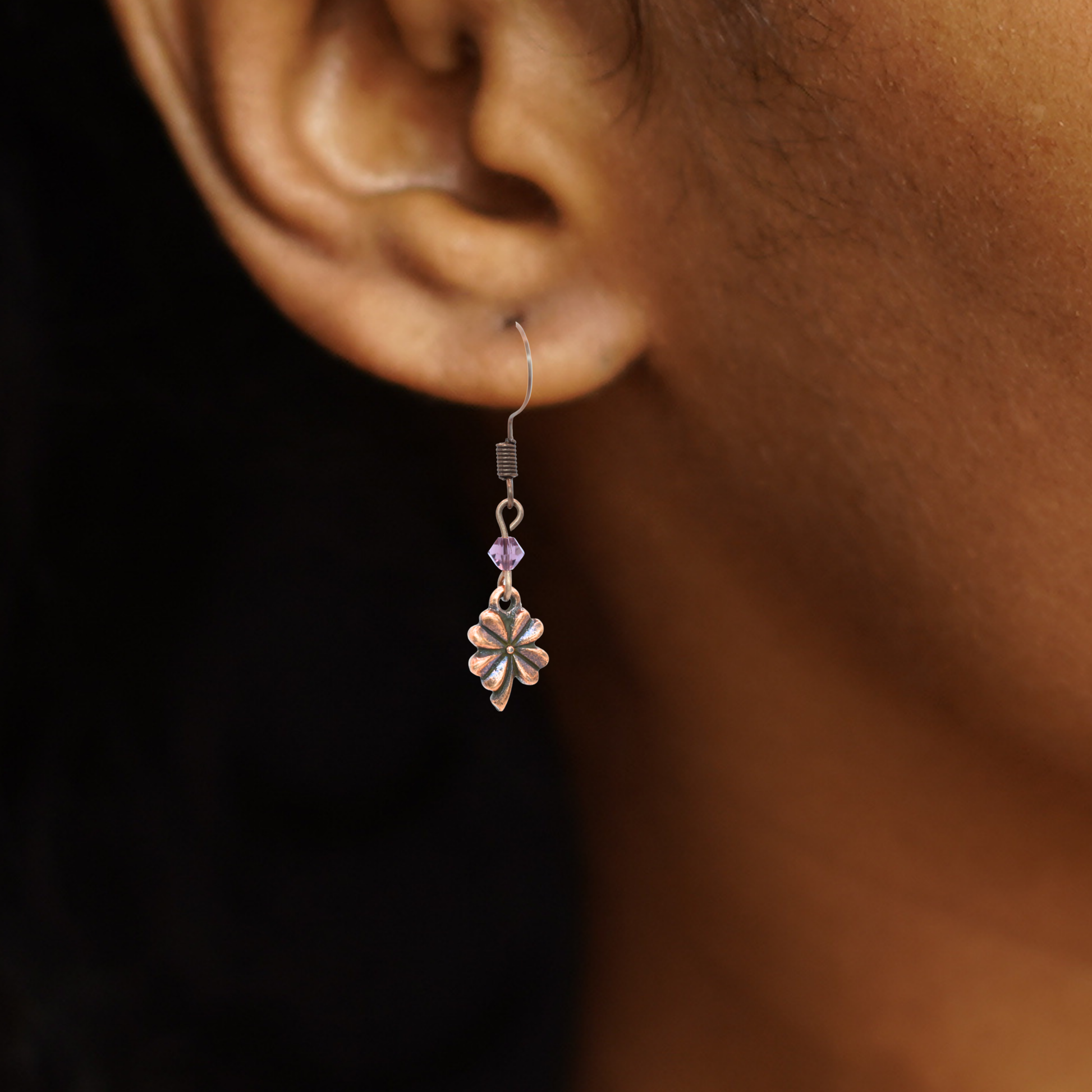 Close up a person wearing earrings featuring antique copper four leaf clover charms and Austrian crystal beads in birthstone colors