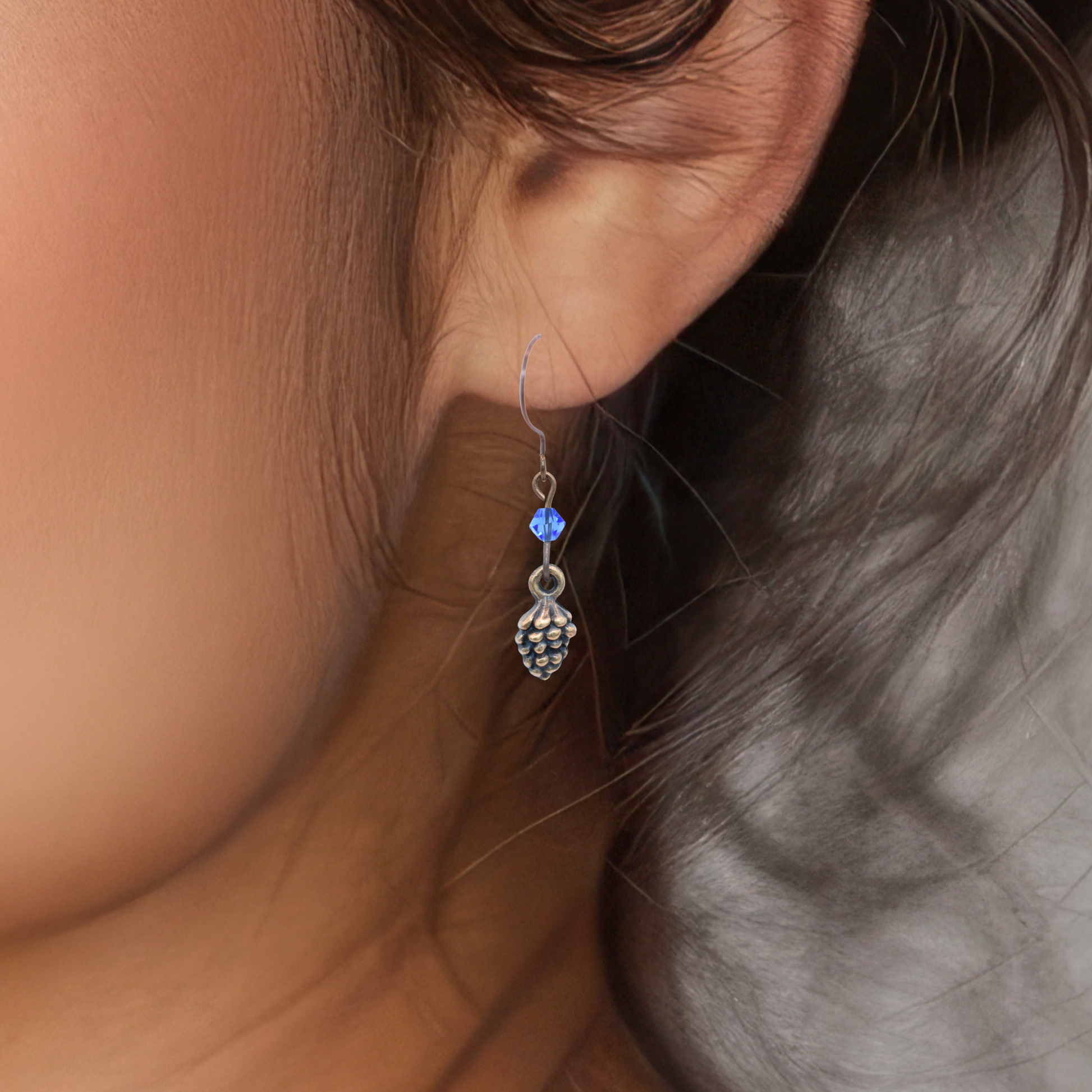 Close-up of an ear wearing an antique copper earring featuring a sapphire blue crystal bead.