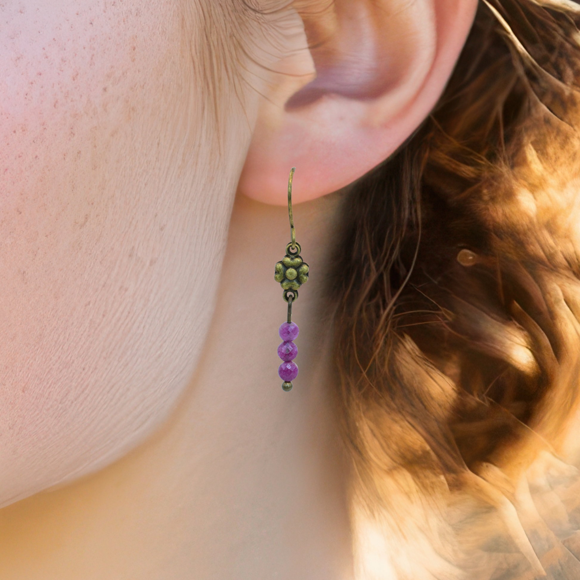 Close-up of an ear wearing an antique bronze flower and ruby beaded earring.