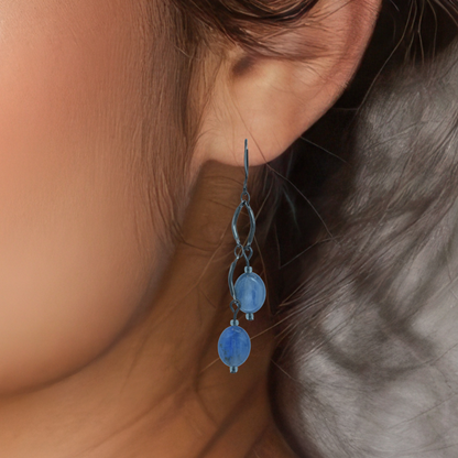 Close-up of a person wearing blue kyanite dangling earrings with a neutral background