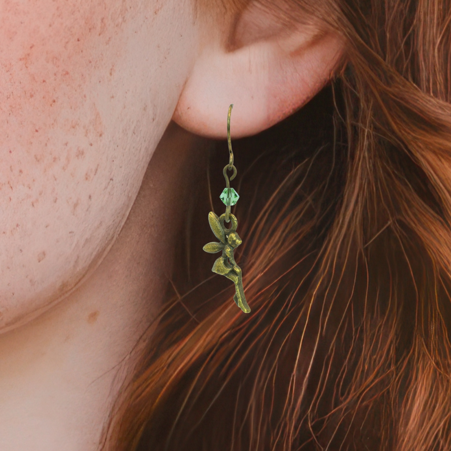 Close-up of a person wearing a fairy-shaped earring with a green crystal bead