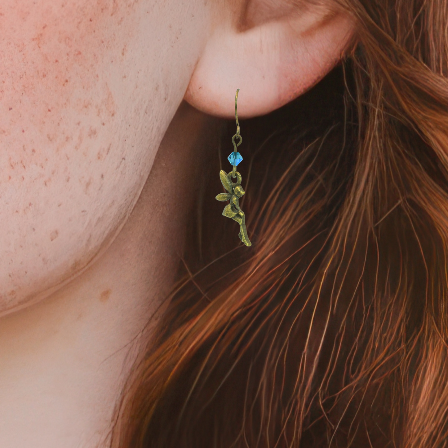 Close-up of an earring with a blue gemstone worn by a person with red hair.