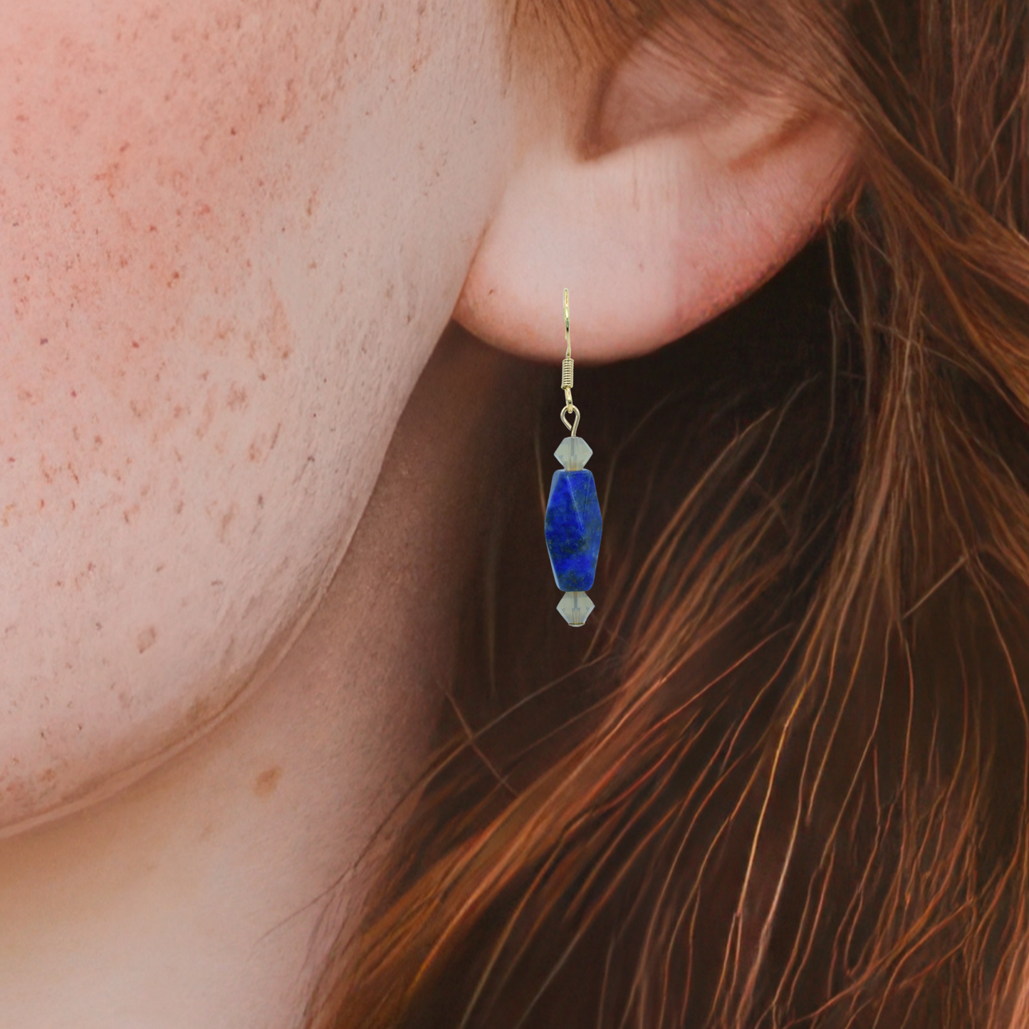 Close-up of an ear wearing a blue lapis earring with gold accents.