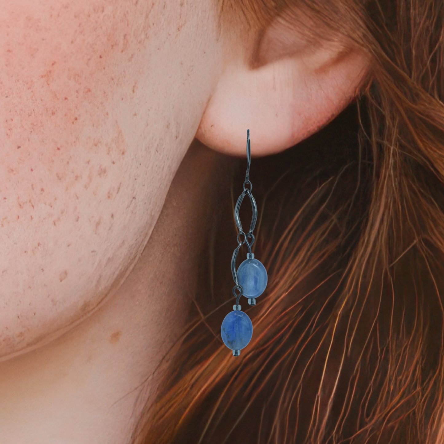 Close-up of an ear wearing a blue dangling earring with brown hair.