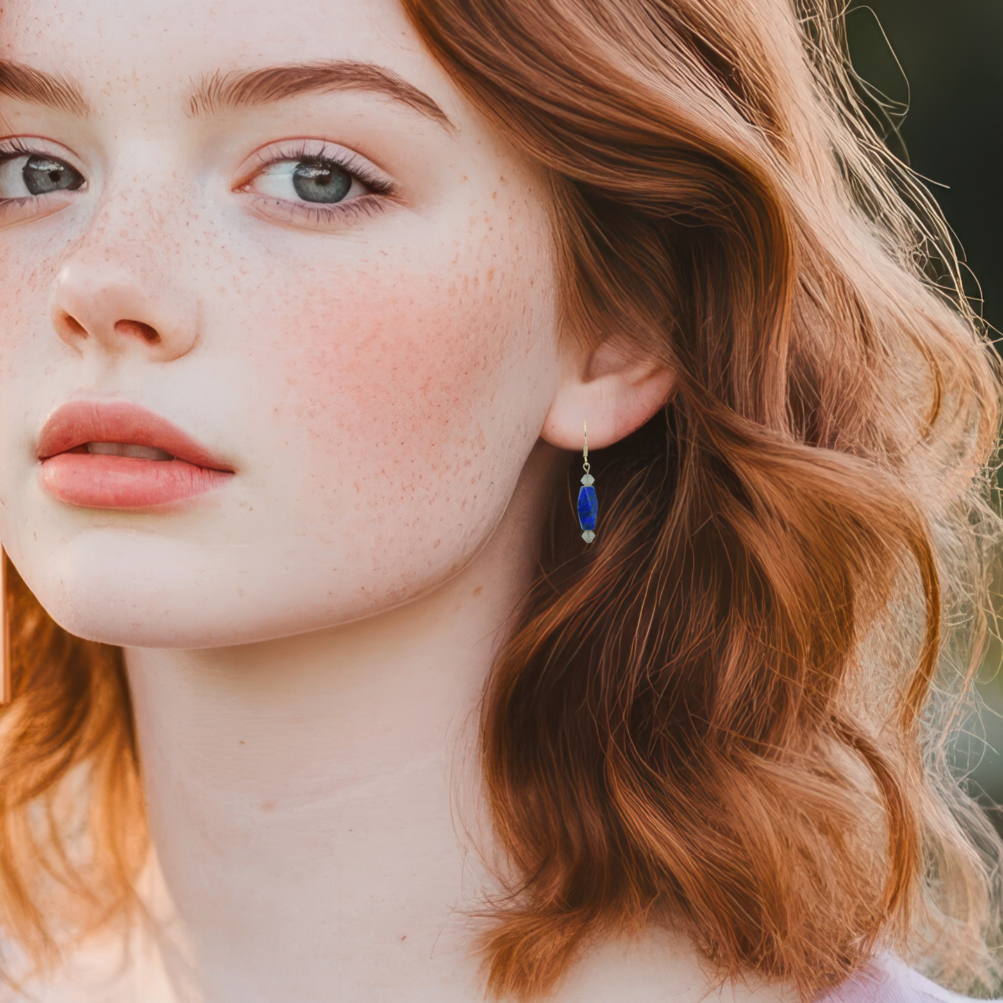 Close-up of a woman with red hair wearing an earring with a blue lapis lazuli gemstone.