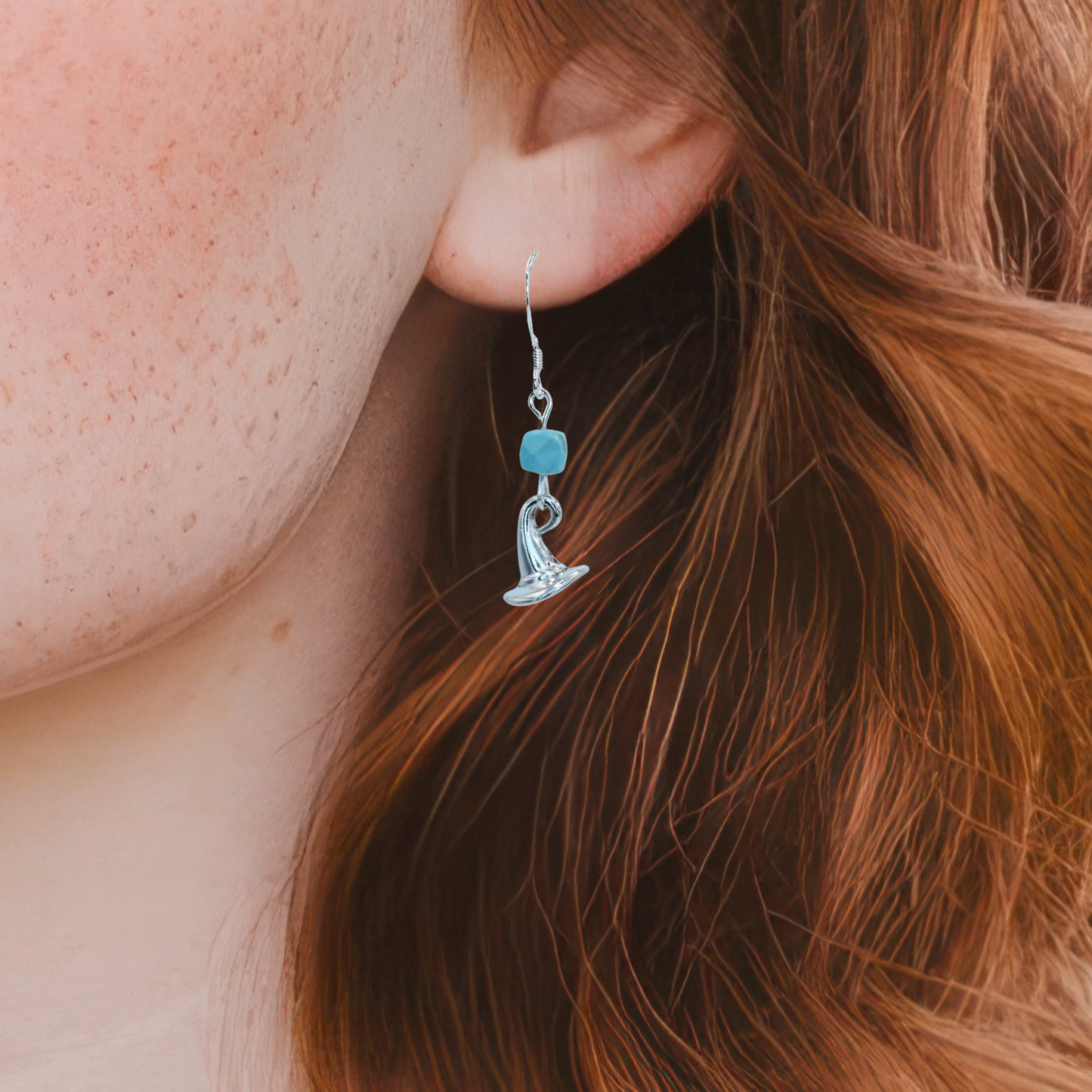 Close-up of a person wearing a silver earring with a blue turquoise gemstone.