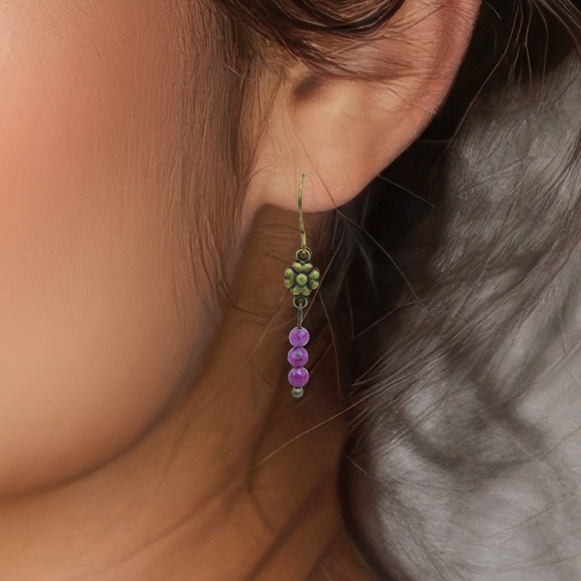 Close-up of an ear wearing a ruby bead earring featuring an antique bronze flower.