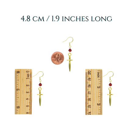 Gold sword-shaped earrings with red beads on a white background, accompanied by two rulers for size reference.