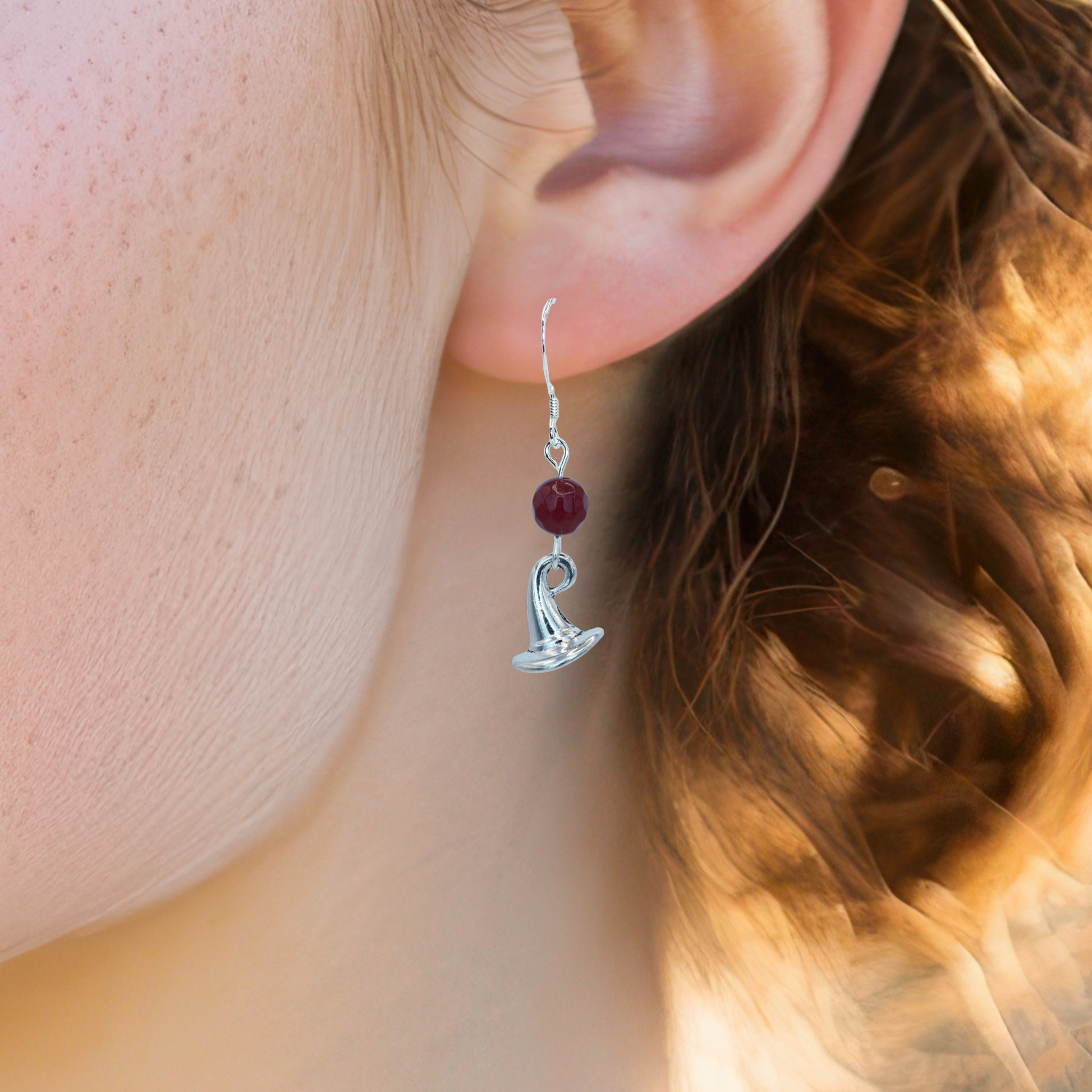 Silver earrings with ruby red jade beads and a wizard hat charm worn by a person