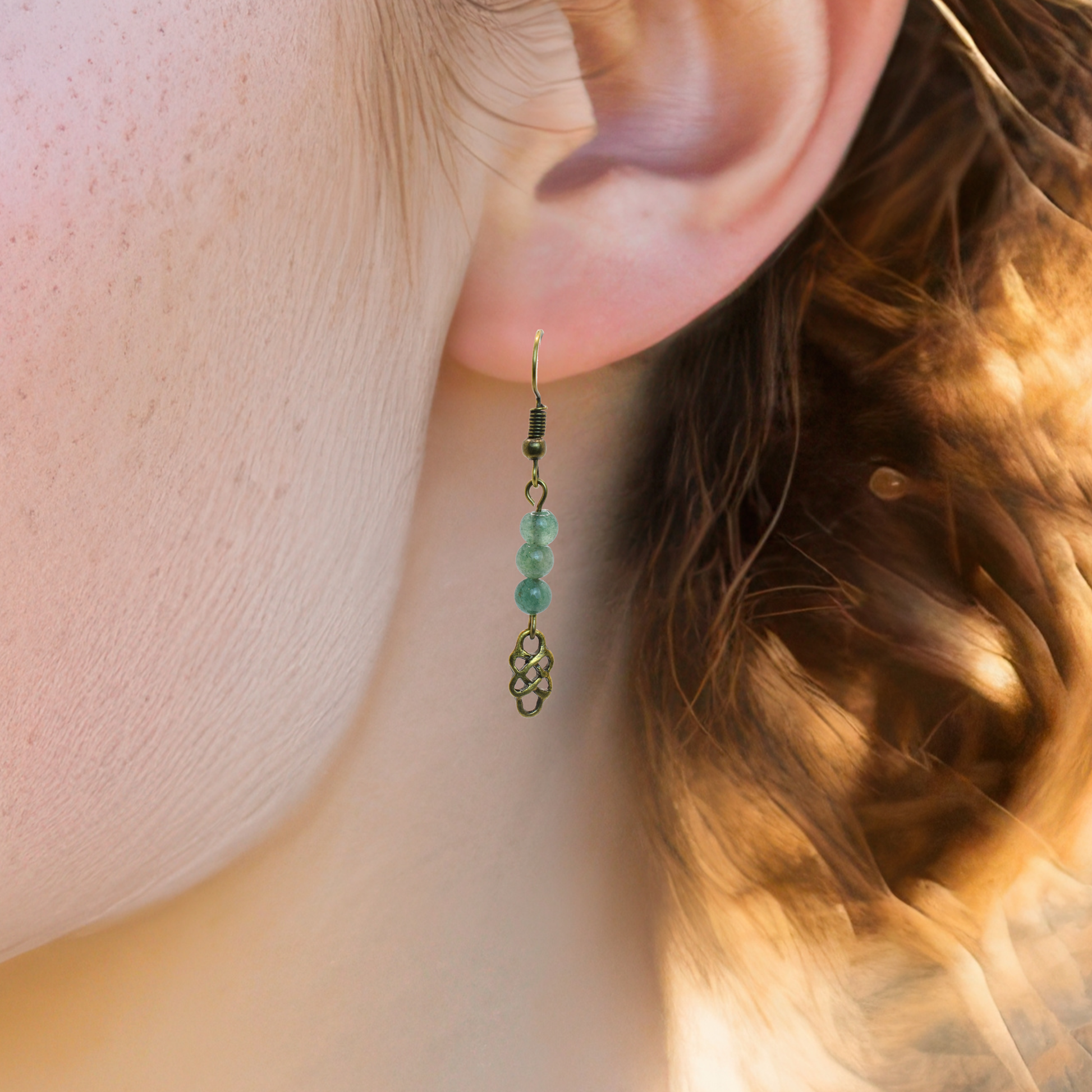 Close-up of an ear wearing a green beaded earring with a blurred background