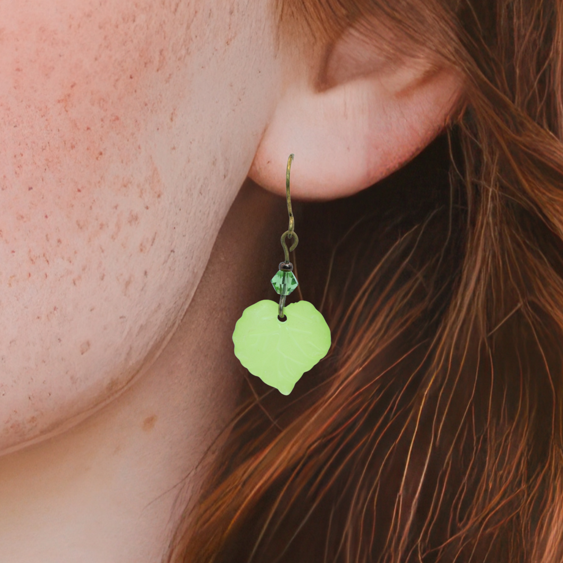 August birthstone green leaf-shaped earring worn by a person with auburn hair.