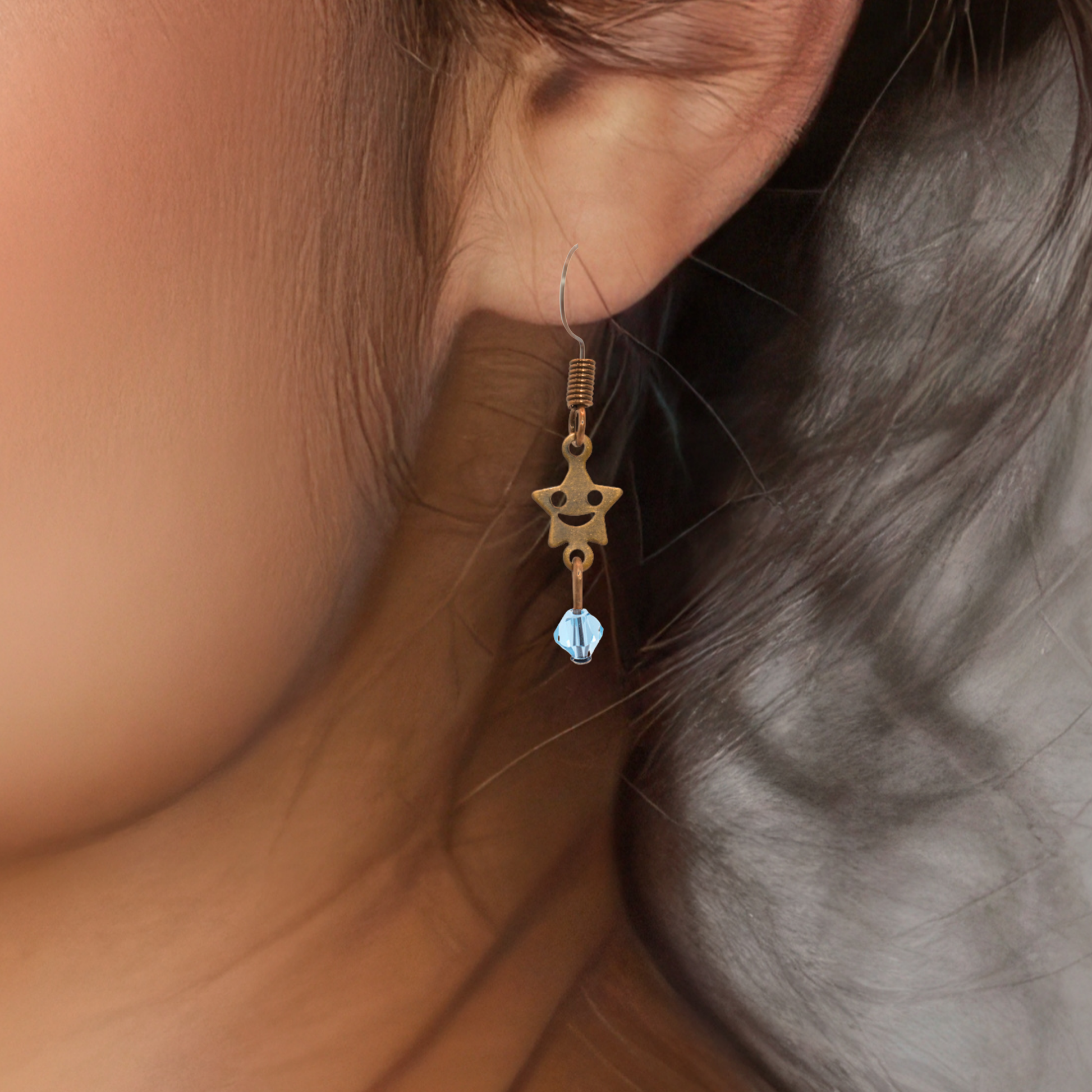 Close-up of an earring with a star-shaped charm and blue gemstone hanging from an ear.