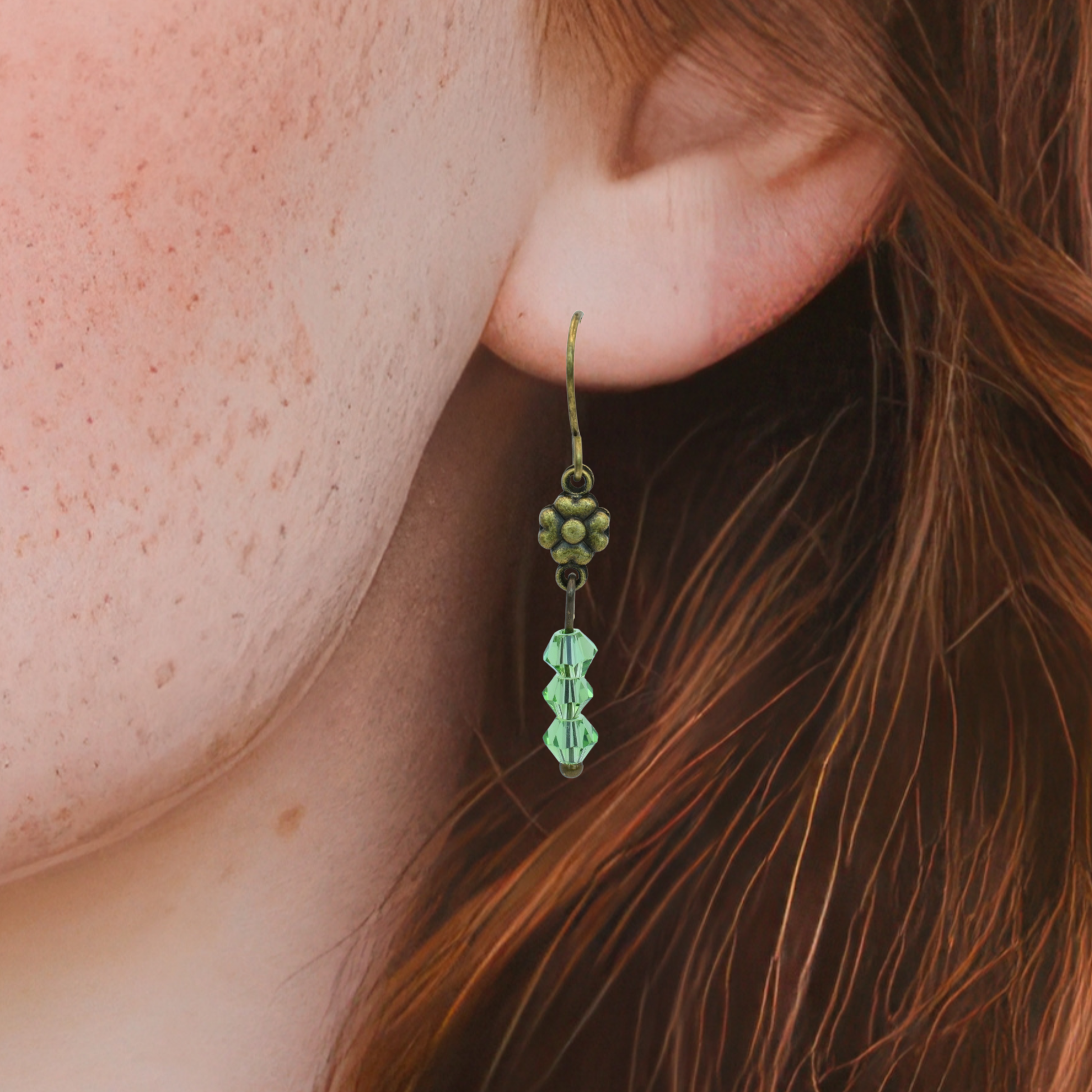 Close-up of a person wearing a green floral earring with a blurred background
