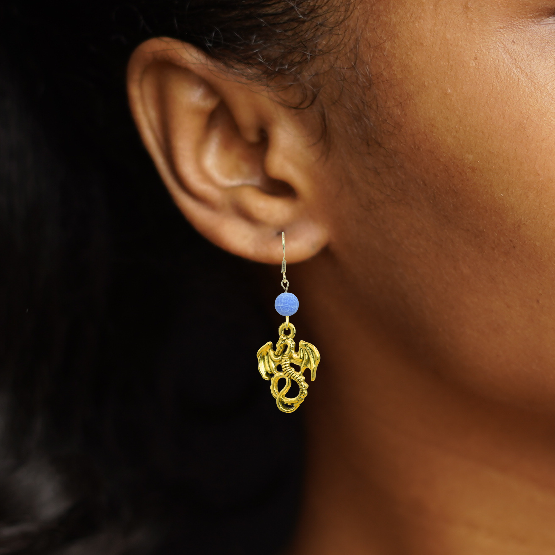 Gold earring with blue bead worn by a person against a dark background