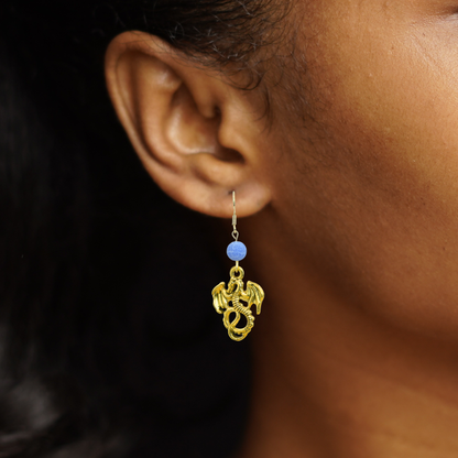 Gold earring with blue bead worn by a person against a dark background
