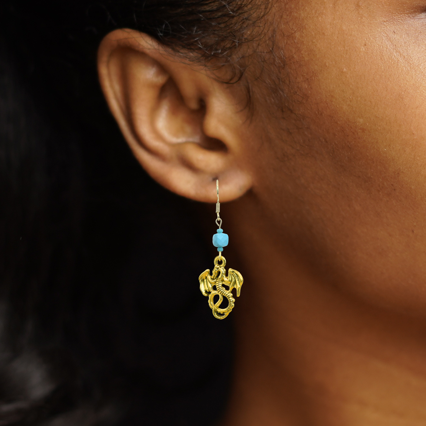 Gold earring with blue bead worn by a person against a dark background