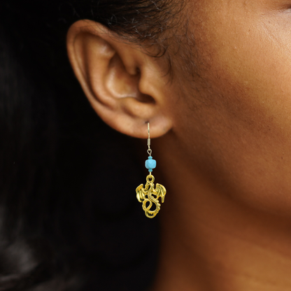 Gold earring with blue bead worn by a person against a dark background