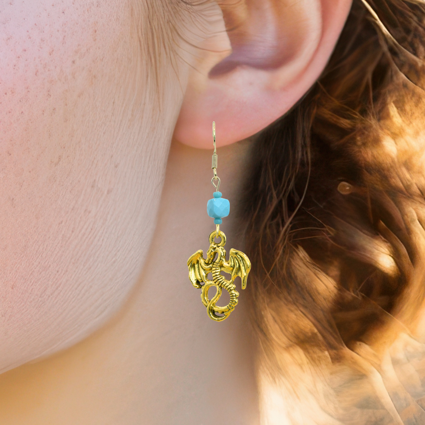 Gold dragon earring with turquoise bead worn by a person