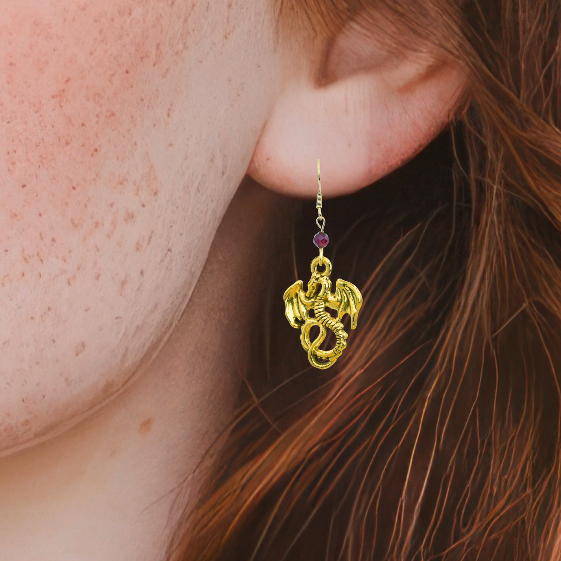 Gold dragon-shaped earring with a red gemstone worn by a person with red hair.