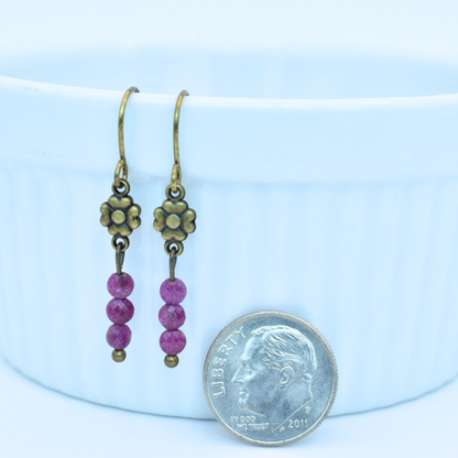 Pair of earrings with pink ruby beads and antique gold accents next to a dime for scale